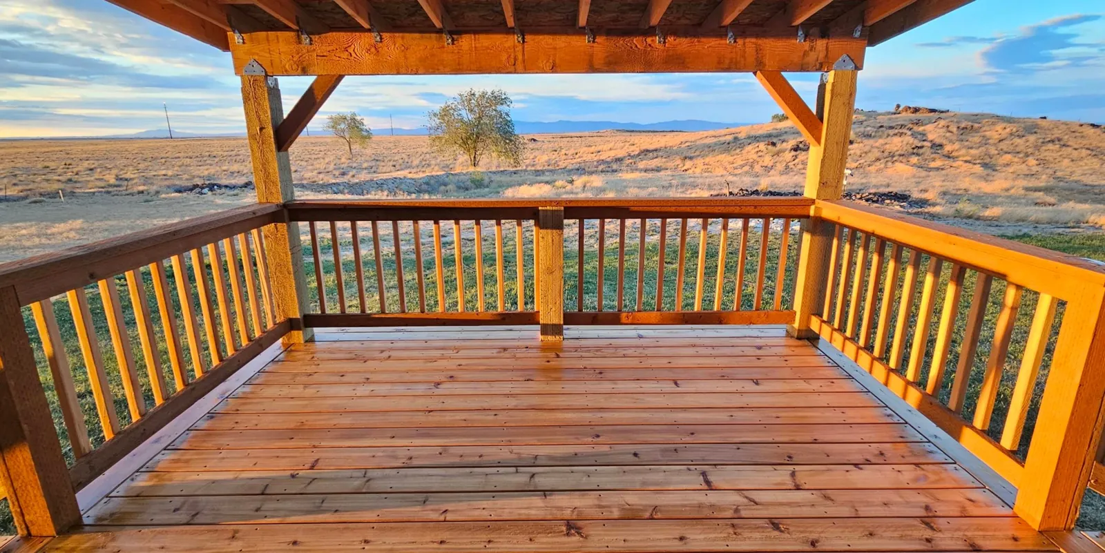 Covered cedar deck with exposed timber roof framing overlooking open land and mountains in Idaho, built by Kemsley Construction