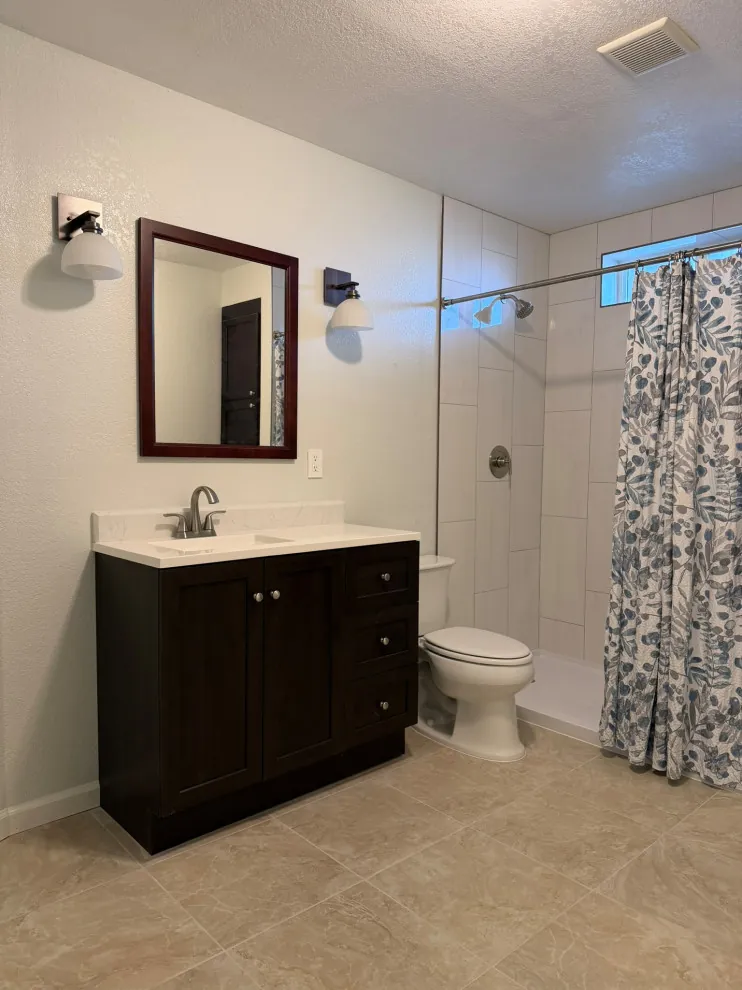 Remodeled bathroom with a dark shaker vanity, quartz top, framed mirror, wall sconces and a tiled walk-in shower in Meridian, Idaho, built by Kemsley Construction